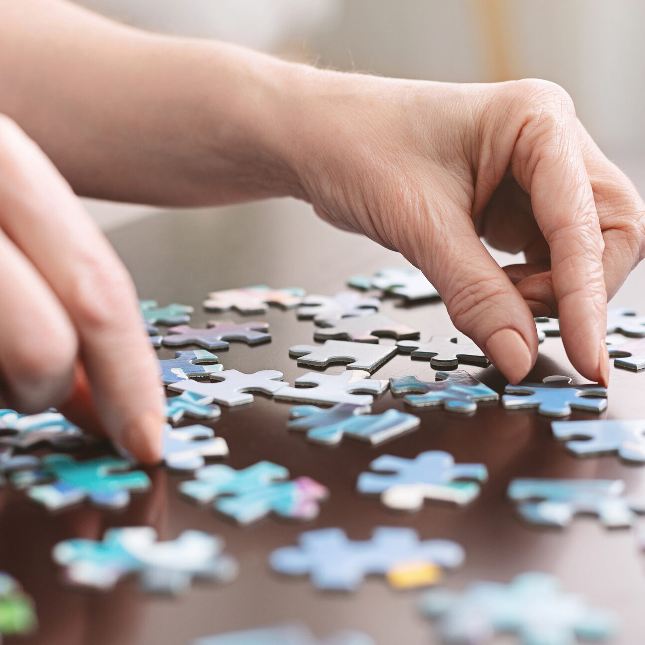 Dementia prevention. Elderly woman hands doing jigsaw puzzle at home, panorama, close up